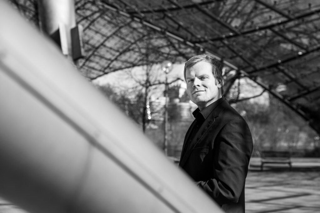 Business Portrait von Mann, der an einer Strebe im Olympiapark lehnt in schwarz-weiss