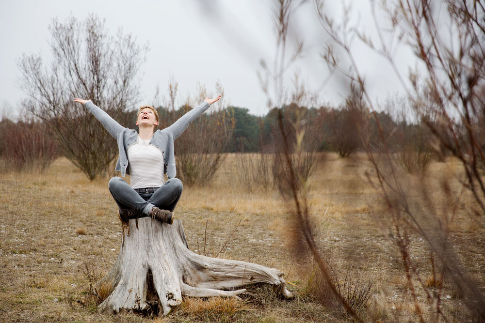 Outdoor Personal Branding Fotos in der Fröttmaninger Heide bei München: Frau sitzt im Schneidersitz auf einem Baumstamm. Das Bild vermittelt ein Gefühl von Freiheit.