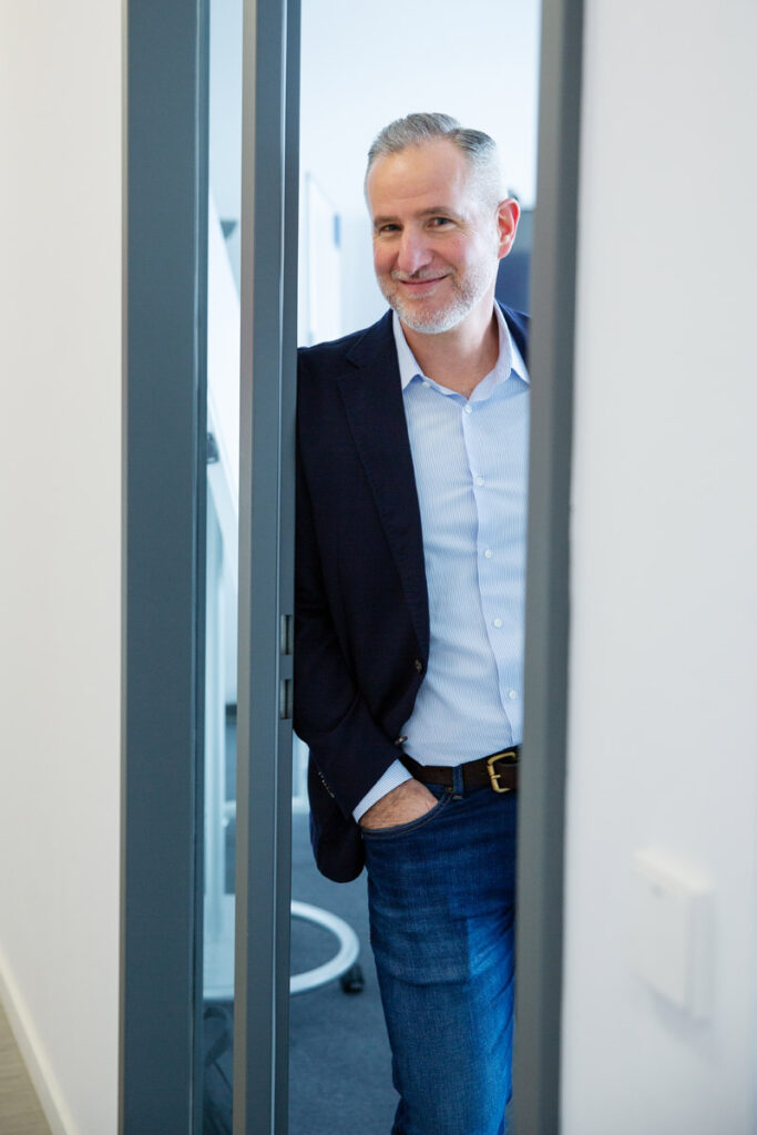 Cooles Corporatefoto von Mitarbeiter, der lässig in der Tür eines Büros in München lehnt.