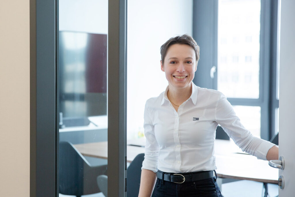 charaktervolles Corporatefoto von Mitarbeiterin einer IT Firma in München, die in der Tür steht und freundlich in die Kamera blickt