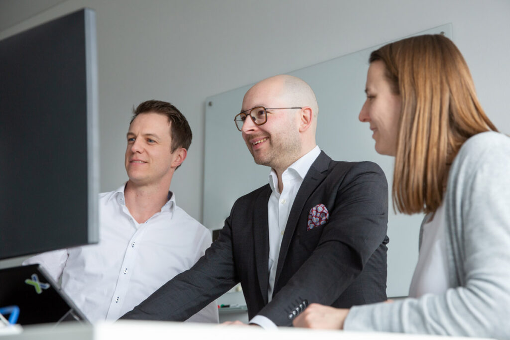 Corporatefotos in München: ein Arbeitsteam aus 3 Personen schuat gemeinsam in einen Bildschirm und bespricht sich.