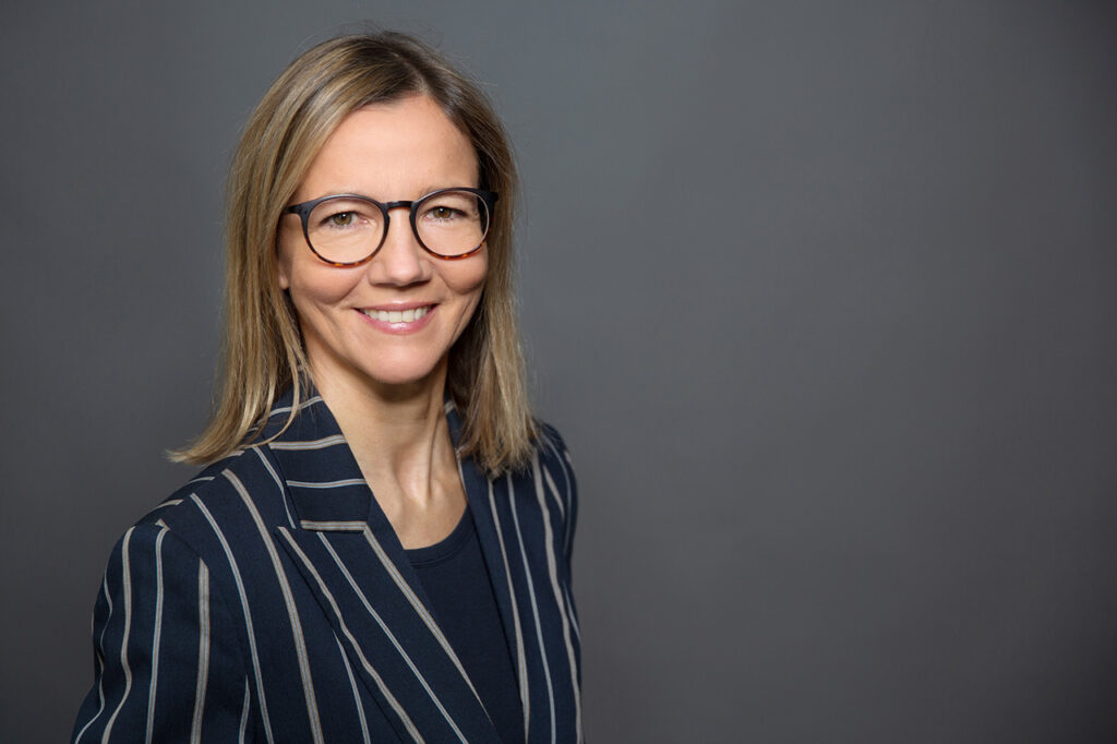 authentisches Mitarbeiterfoto von Frau vor neutralem Studiohintergrund