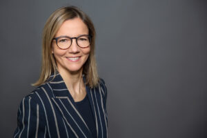 authentisches Mitarbeiterfoto von Frau vor neutralem Studiohintergrund