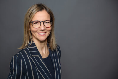 authentisches Mitarbeiterfoto von Frau vor neutralem Studiohintergrund