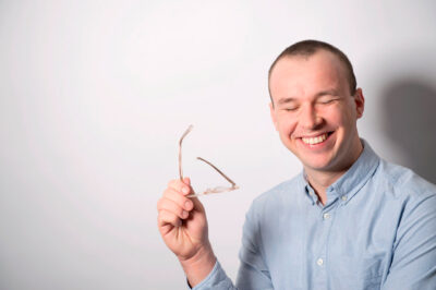 lachendes Autorportrait mit Brille im Fotostuio mit wiessem Hintergrund.