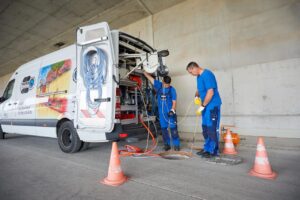 Baustellenfotografie: zwei Kanalarbeiter auf der Autobahn Lindau-München mit ihrem Transporter vor einem Kanalschacht.