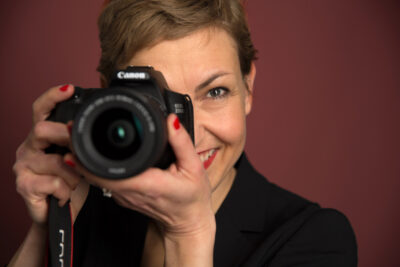 Businessfoto von Frau mit Kamera vor rotem Hintergrund im Fotostudio