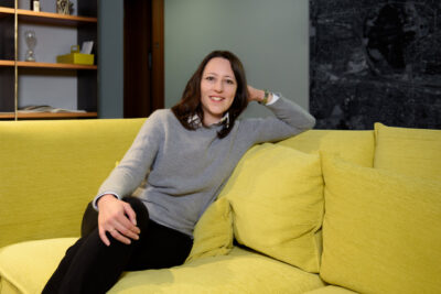 Modernes Businessportrait einer Unternehmerin, die lächelnd auf einer Couch im Büro sitzt.