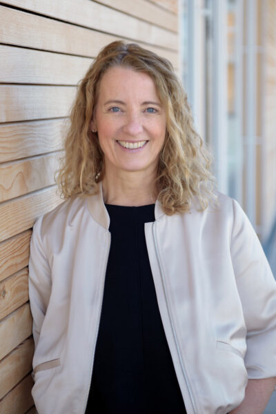 Personal-Branding-Fotografie: Natürliches Businessportrait einer Schulleiterin fotografiert vor ihrer Schule mit unscharfem Hintergrund.