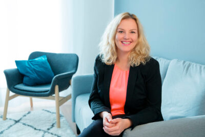 Authentisches Businessportrait: junge Unternhemerin sitzt lächelnd auf einer Couch in ihrem Geschäftsraum.