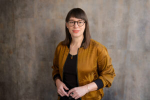 Cooles Bewerbungsfoto: Frau in Casual-Outfit steht vor strukturiertem Hintergund, fotografiert im Fotostudio in München mit Tageslicht.