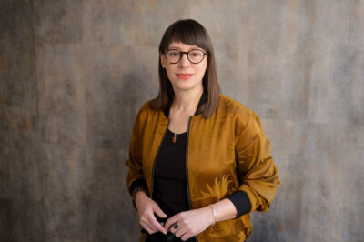 Cooles Bewerbungsfoto: Frau in Casual-Outfit steht vor strukturiertem Hintergund, fotografiert im Fotostudio in München mit Tageslicht.