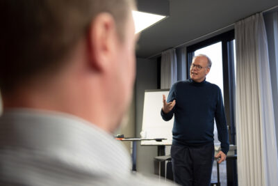 Corporate Fotografie von Führungskräfte-Coaching: Referent spricht zugewandt zu den TeilnehrmerInnen.