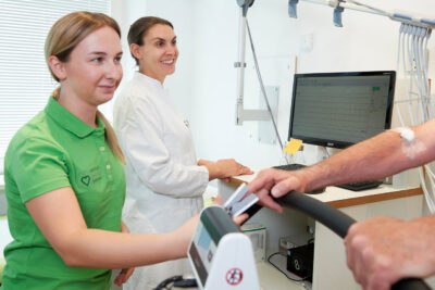 Corporate Fotografie in Arztpraxis. Im Vordergrund ist ein Patient zu erahnen, im Fokus sind zwei Perosnen lächelnd im Gespräch mit dem Patienten.