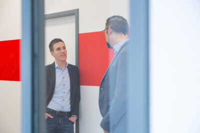 Employer Branding Fotografie: Zwei Kollegen sind auf dem Gang des Büros in ein Gespräch vertieft.