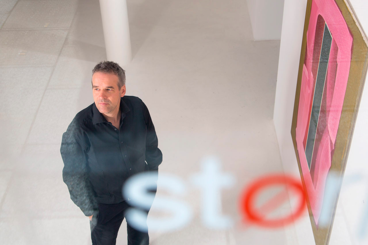 Kreatives Künstleportrait: Stephan Stumpf in seiner Galerie in München-Schwabing, mit unscharfem Logo im Vordergrund