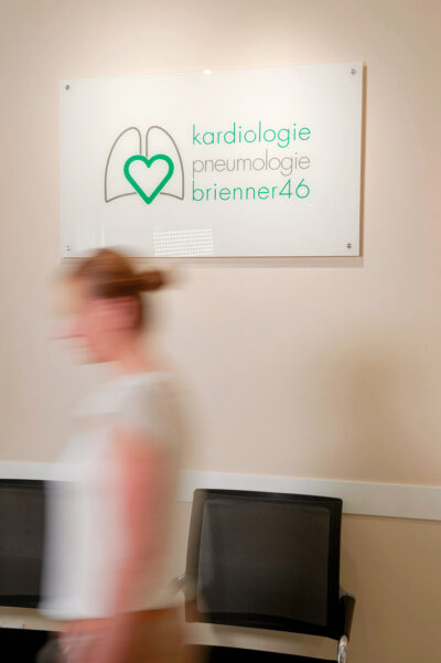 Lebendiges Employer Branding Foto für eine kardiologische Praxis in München. Vor dem Praxisschild geht eine Frau vorbei, die unscharf ist.