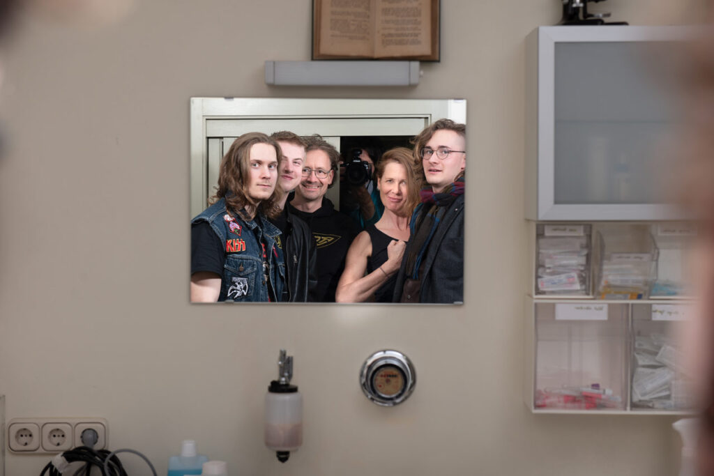 Bandfoto von Defibrüllator. Portraitaufnahme der Bandmitglieder in einem Spiegel einer Arztprraxis