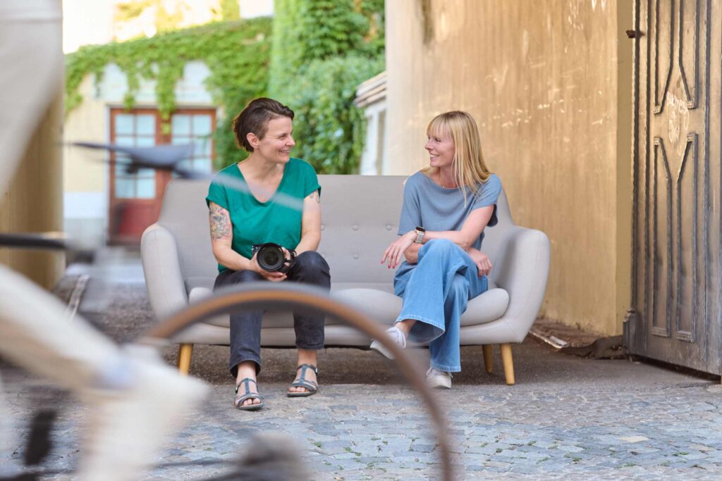 Businessfotografinnen Alice Vogel und Barbara Andres auf einer Couch vor dem Fotostudio in München Maxvorstadt